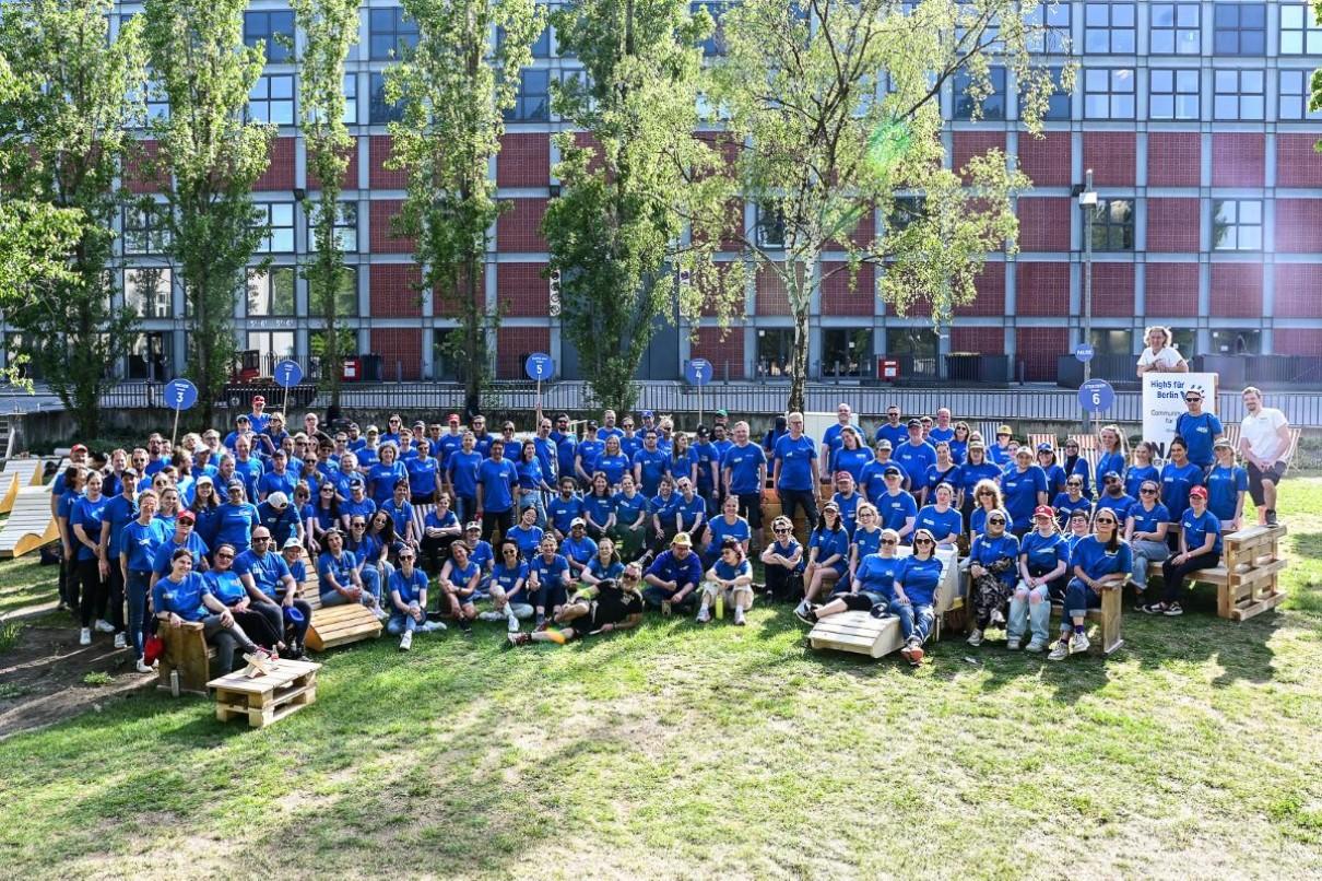 Auf dem Bild sind 150 Messe Berliner:innen auf dem Rasen stehend zu sehen, die blaue Messe Berlin T-Shirts tragen.